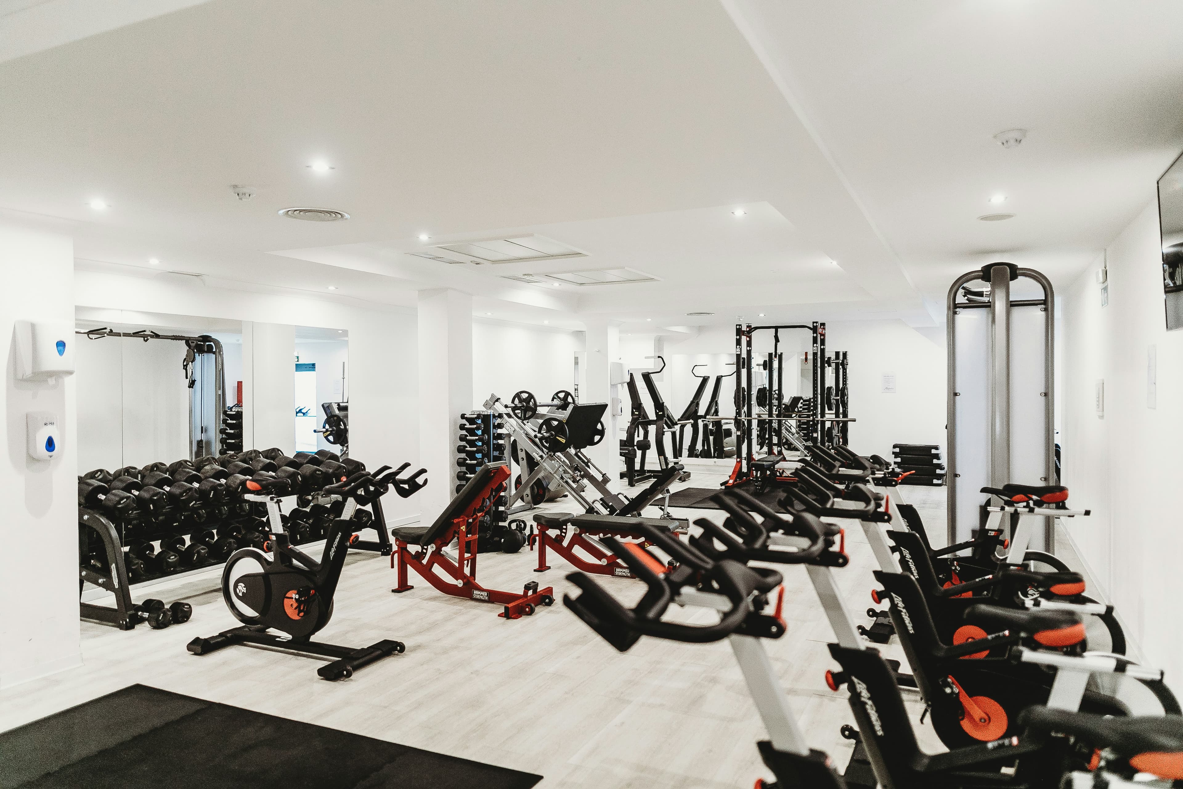 Gimnasio vacío, con bicicletas, bancos y un rack de mancuernas.