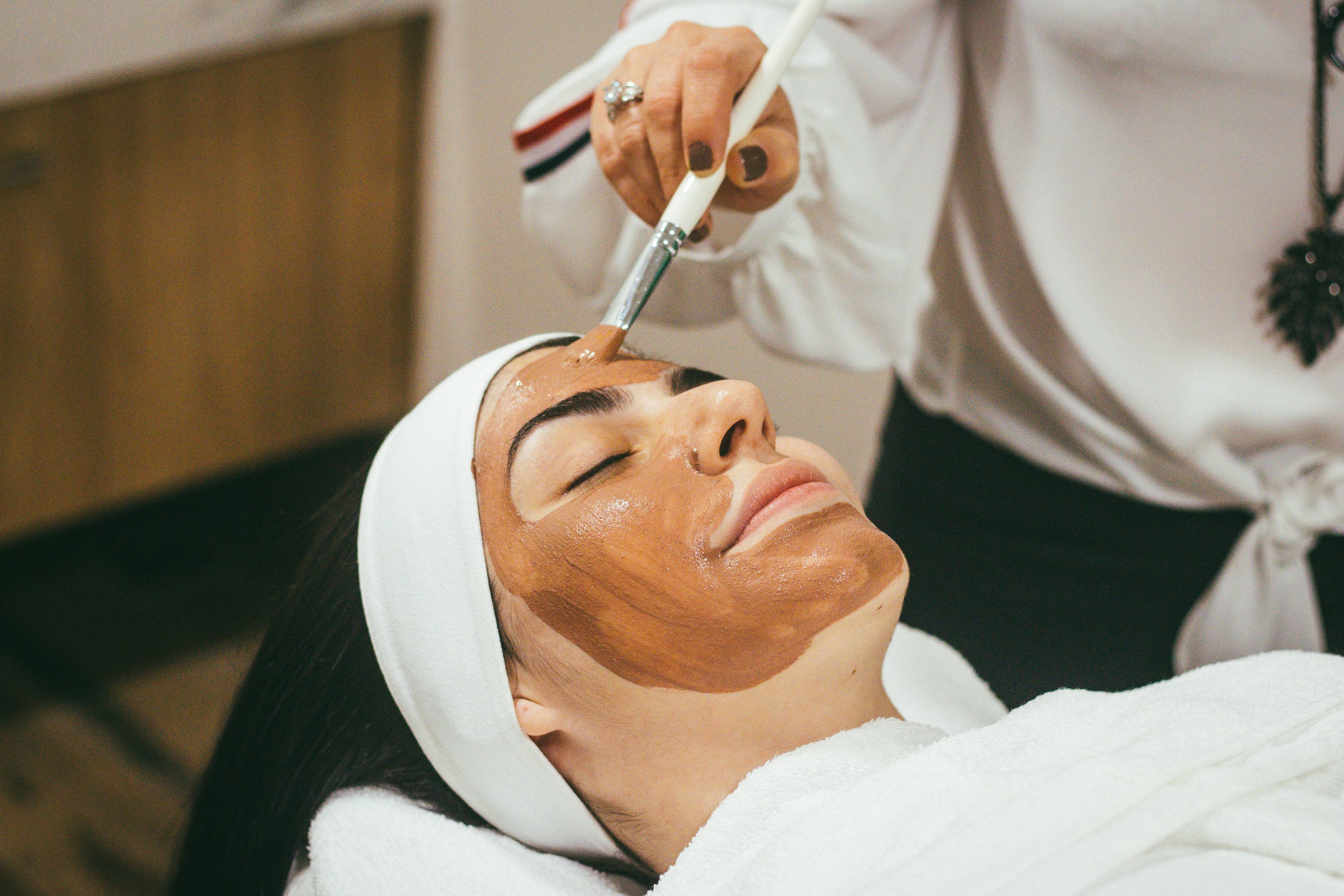 Esteticista aplicando una mascarilla con una brocha a una clienta tumbada.