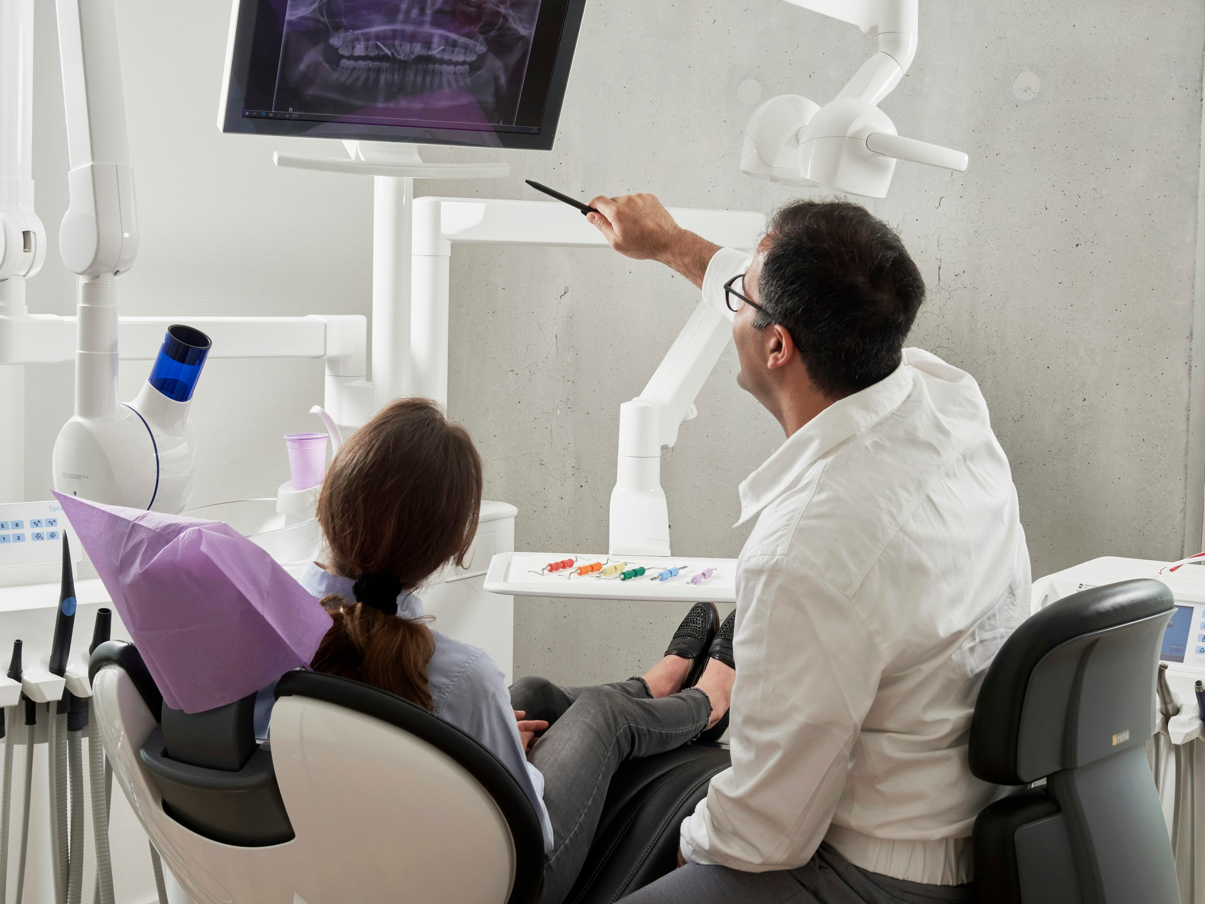 Dentista mostrando una radiografía en pantalla a una paciente sentada en el sillón.