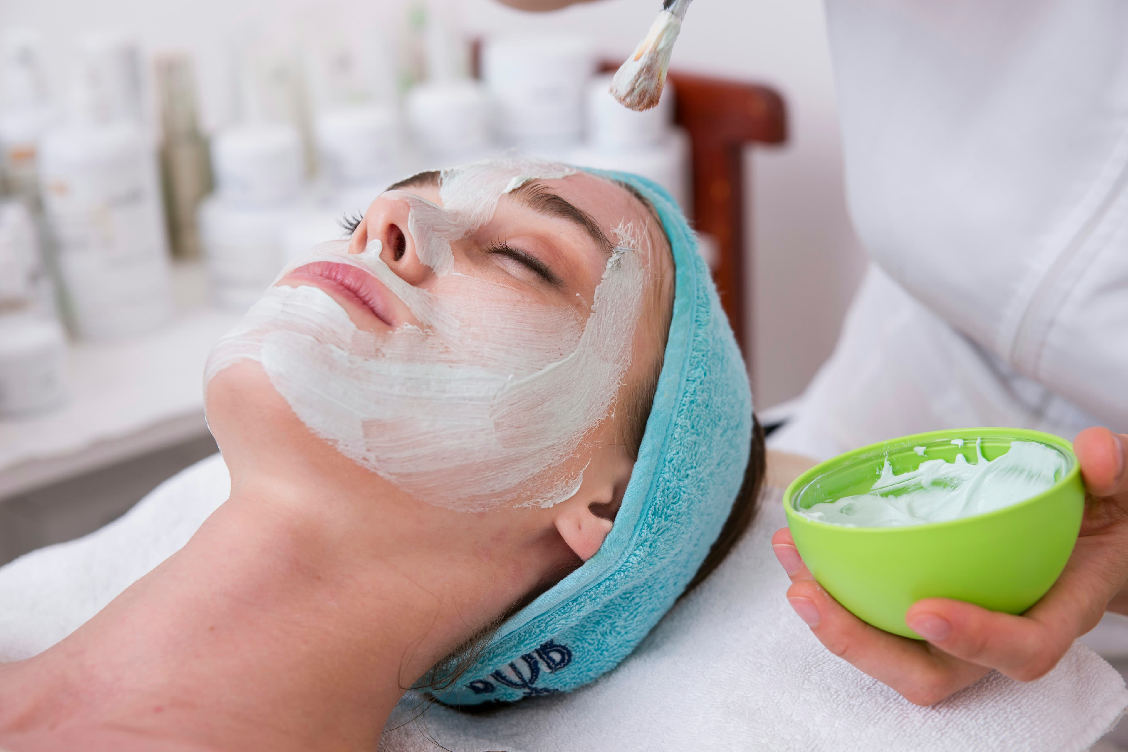 Tratamiento facial en curso, con una mascarilla blanca y un cuenco de producto.