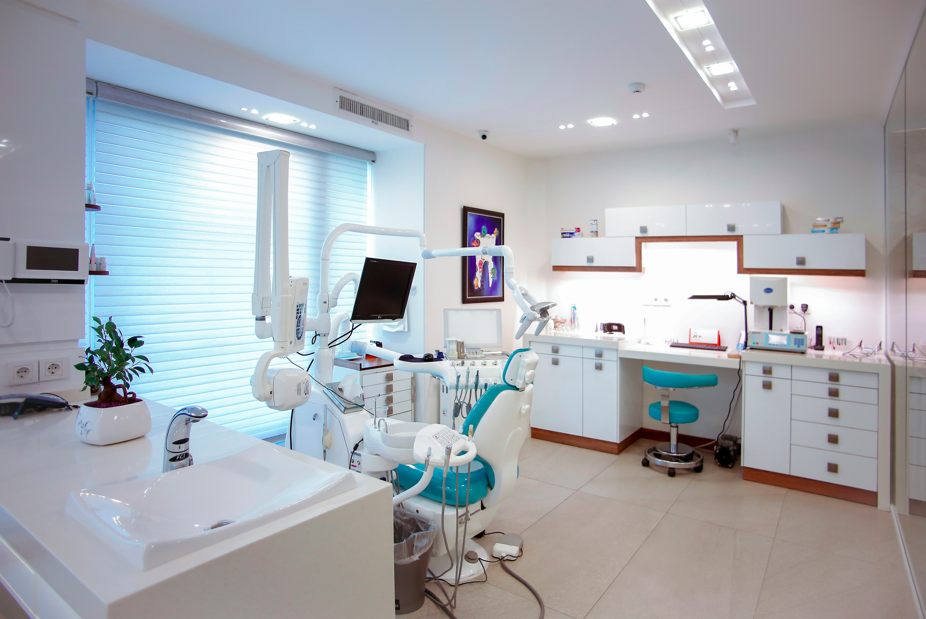 Gabinete dental vacío, con el sillón, la lámpara y el lavabo junto a una ventana.